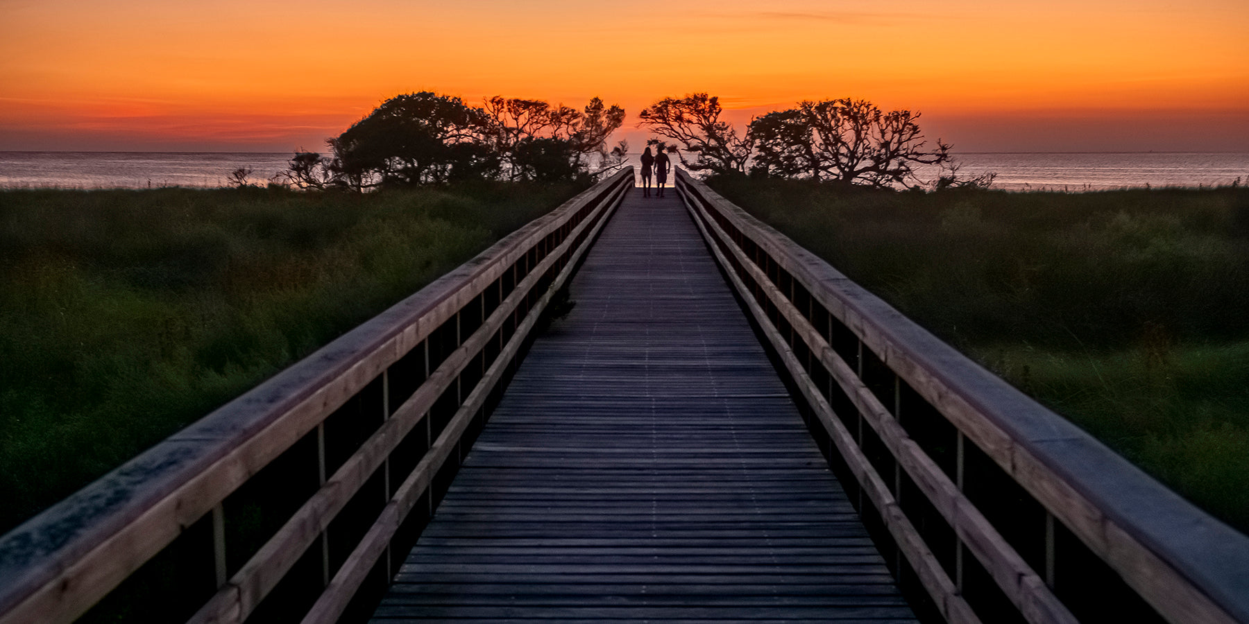 A couple stroll to the water at sunset